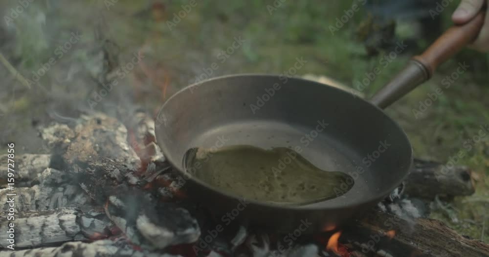 Man spreads oil frying pan on campfire Man spreads oil frying pan on campfire