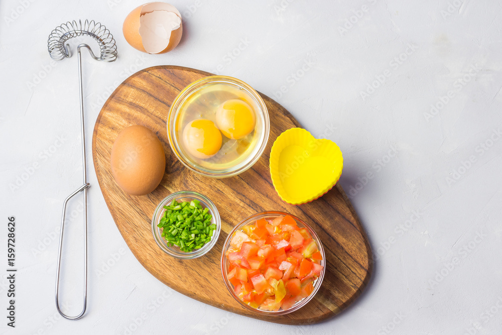 Ingredients for egg mini frittatas on wooden board - tomatoes, scallions, eggs. Top view. Ingredients for egg mini frittatas on wooden board - tomatoes, scallions, eggs. Top view.