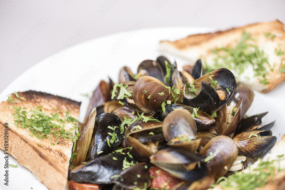 Mussels in sauce with parsley, French toast and lemon. Seafood. Clams in the shells. Delicious snack for gourmands. Isolated on light background, white plate