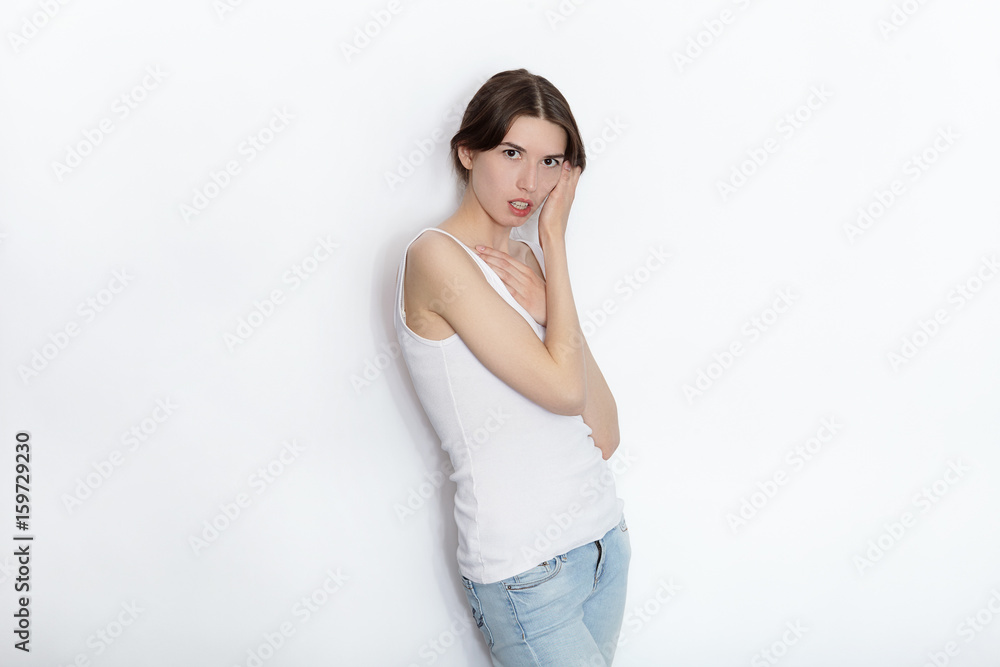 Young beautiful brunette beginner model woman in white t-shirt blue jeans practicing posing showing emotions on white wall studio background Young beautiful brunette beginner model woman in white t-shirt blue jeans practicing posing showing emotions on white wall studio background