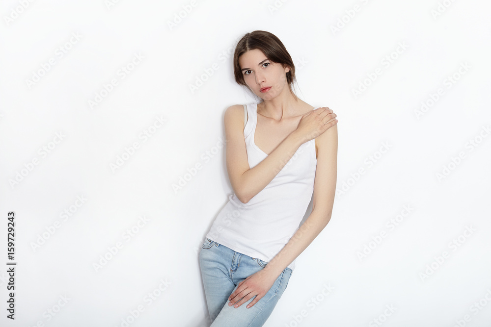 Young beautiful brunette beginner model woman in white t-shirt blue jeans practicing posing showing emotions on white wall studio background Young beautiful brunette beginner model woman in white t-shirt blue jeans practicing posing showing emotions on white wall studio background