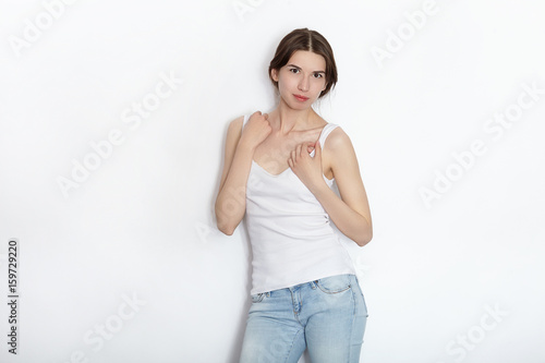 Young beautiful brunette beginner model woman in white t-shirt blue jeans practicing posing showing emotions on white wall studio background