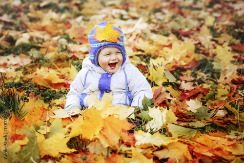 the laughing boy sits on autumn leaves in the city park