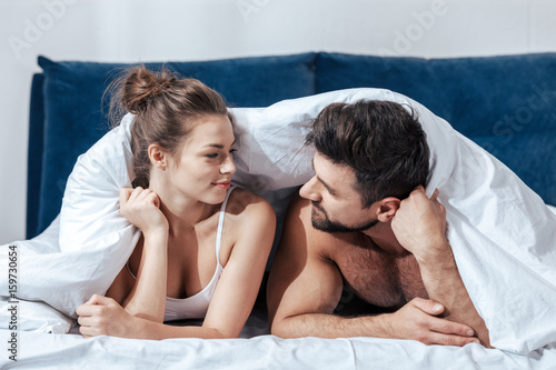 Portrait of young happy loving couple under blanket in bed