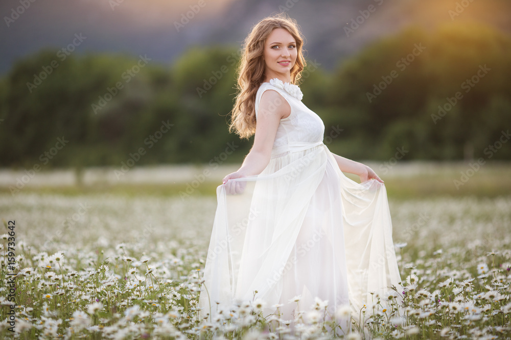 Beautiful happy pregnant girl on the field of daisy flowers, sunset time Beautiful happy pregnant girl on the field of daisy flowers, sunset time