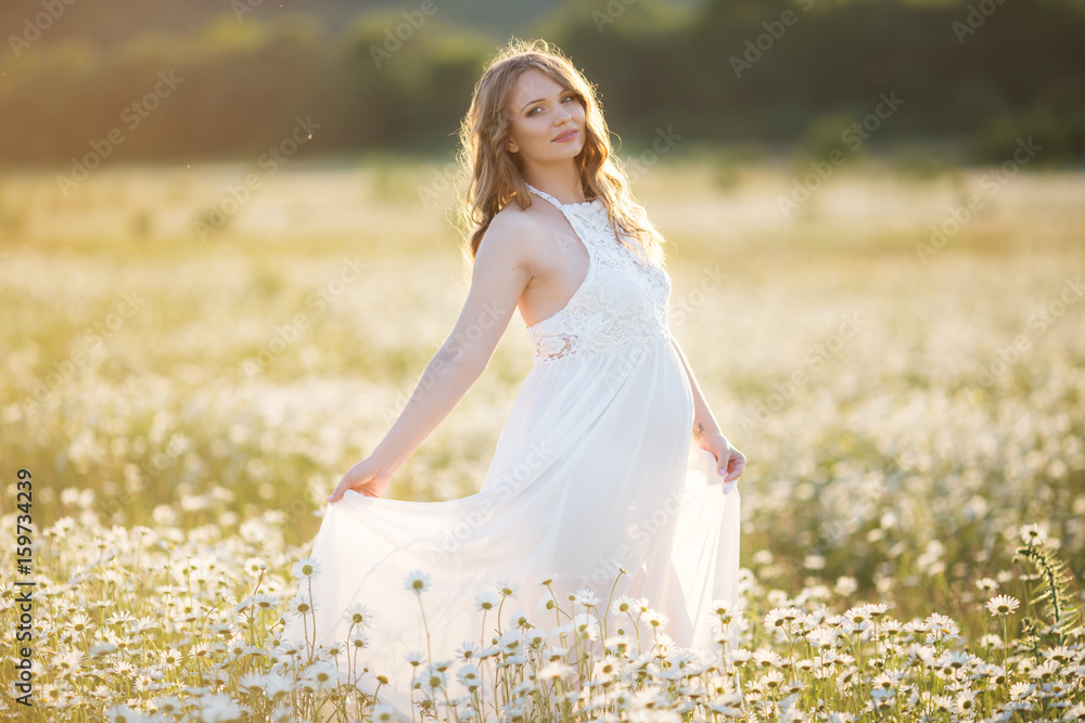 Beautiful happy pregnant girl on the field of daisy flowers in sunset lights Beautiful happy pregnant girl on the field of daisy flowers in sunset lights