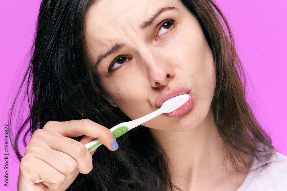 Woman brushing her teeth on a pink background portrait Woman brushing her teeth on a pink background portrait