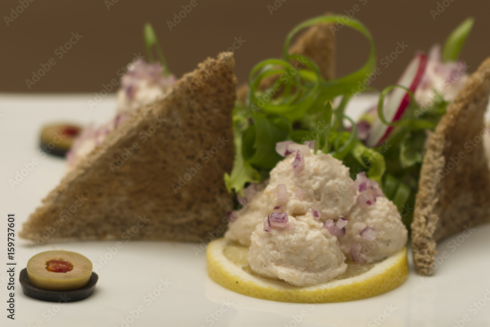 Fish roe salad, whit toasted bread, onion, green leafs, lemon, radish and olives, placed on a white plate, brown background Fish roe salad, whit toasted bread, onion, green leafs, lemon, radish and olives, placed on a white plate, brown background