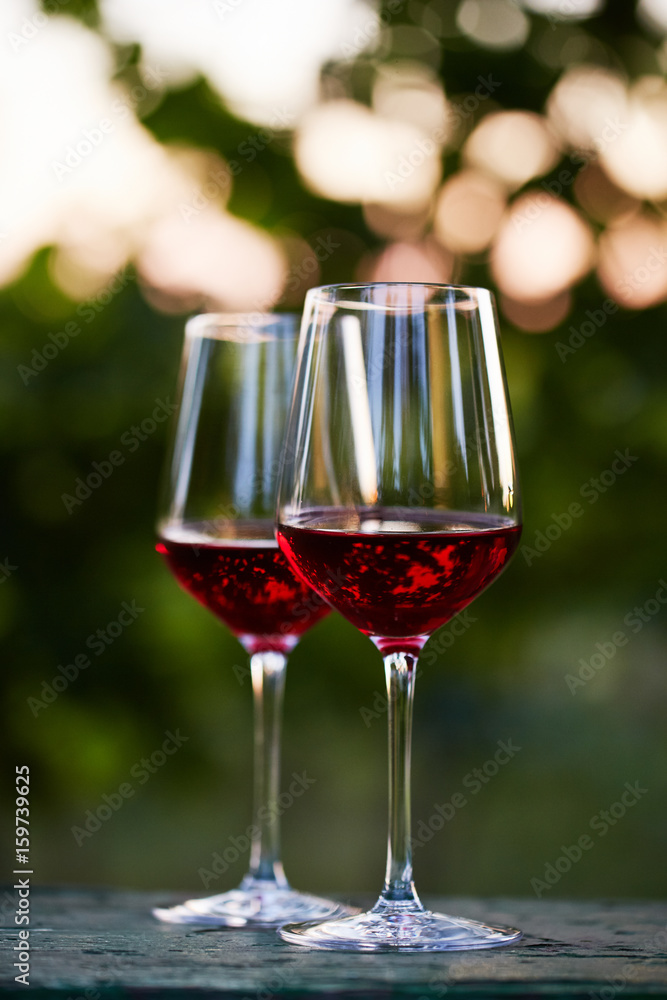 Two glasses of red wine on table in the vineyard at sunset