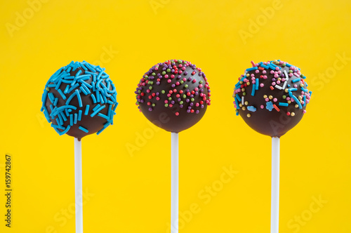 Chocolate cake pops decorated with colorfull confectionery sprinkles on a yellow background. Picture for a menu or a confectionery catalog.