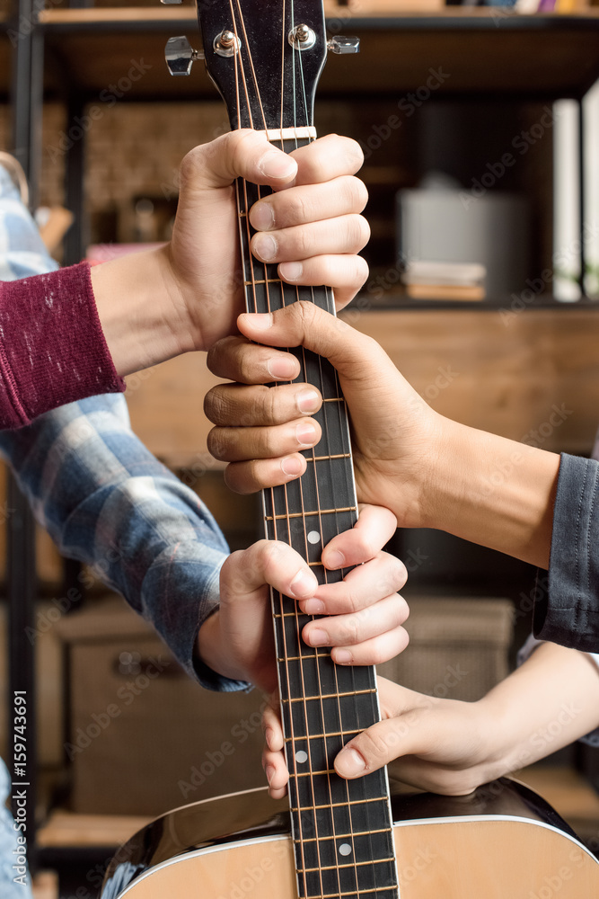 cropped view of teenagers holding guitar fretboard at home, teenagers playing guitar concept cropped view of teenagers holding guitar fretboard at home, teenagers playing guitar concept