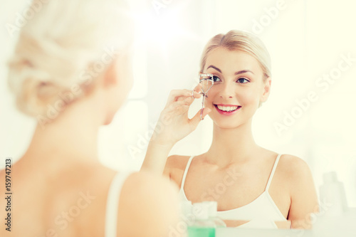 woman with curler curling eyelashes at bathroom