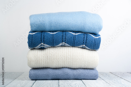 Knitted wool sweaters. Pile of knitted winter, autumn clothes on white, wooden background, sweaters, knitwear, space for text