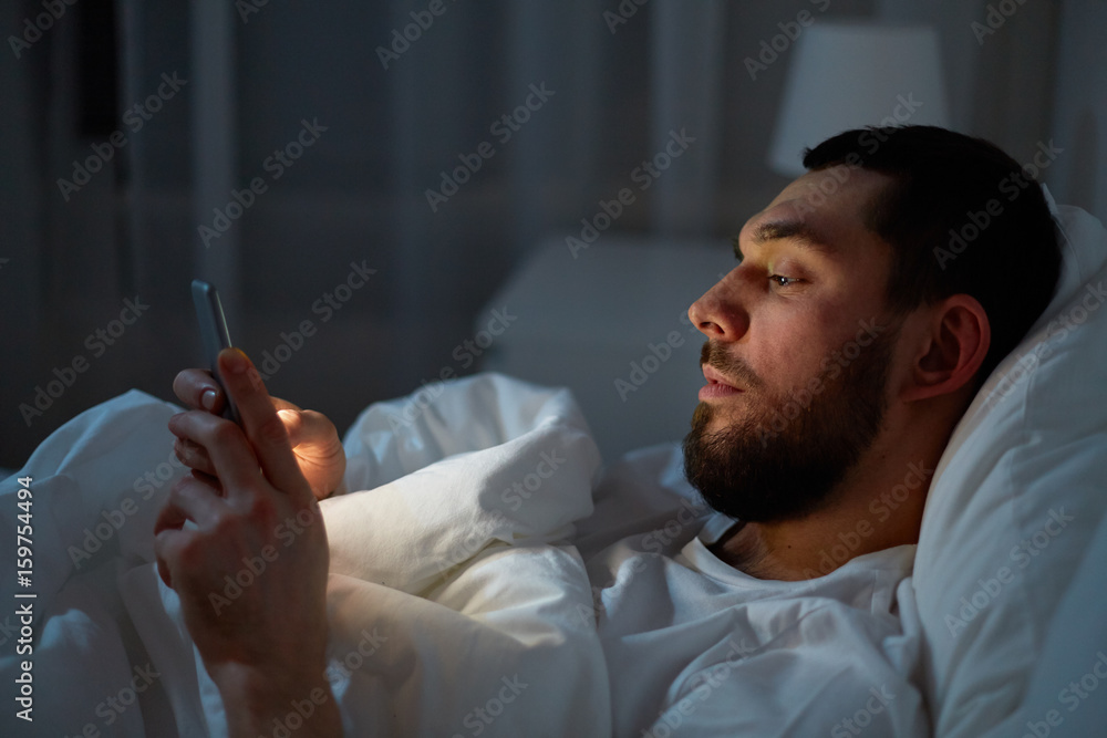 Fototapeta premium man with smartphone in bed at night