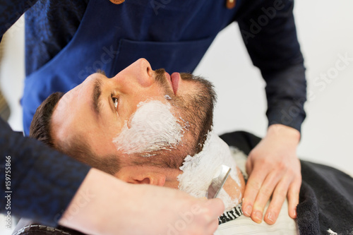 man and barber with straight razor shaving beard photo