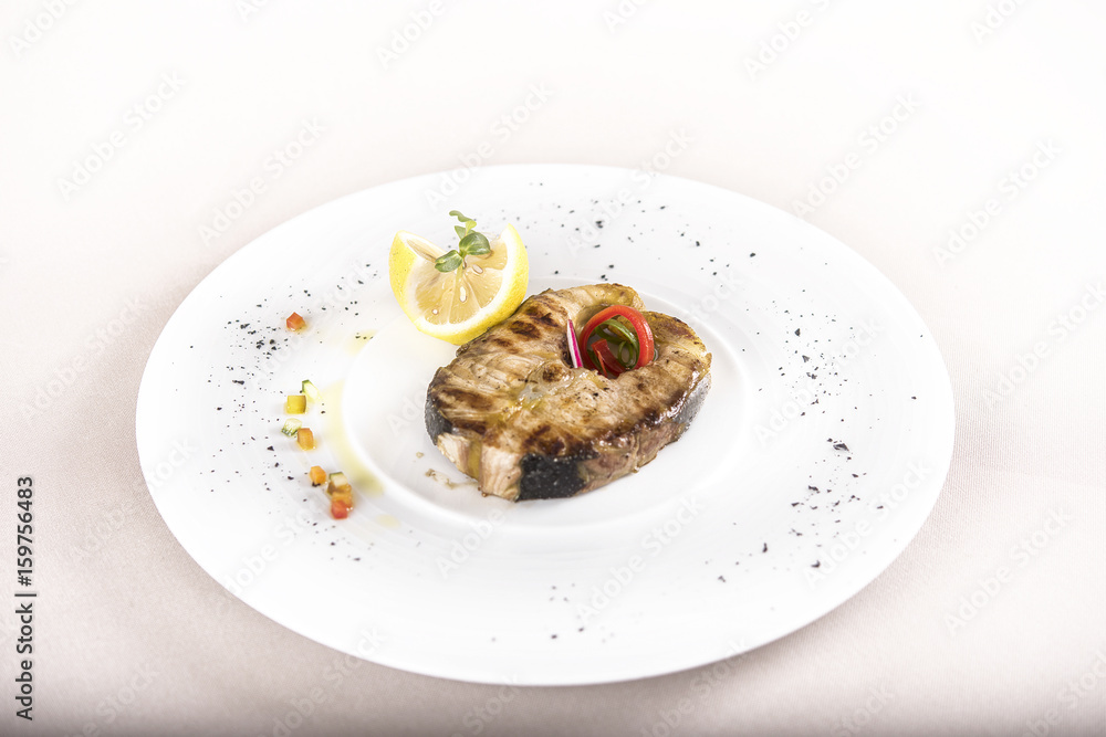 Grilled carp, served with lemon and decorated with radish and fresh leafs, light background, isolated Grilled carp, served with lemon and decorated with radish and fresh leafs, light background, isolated