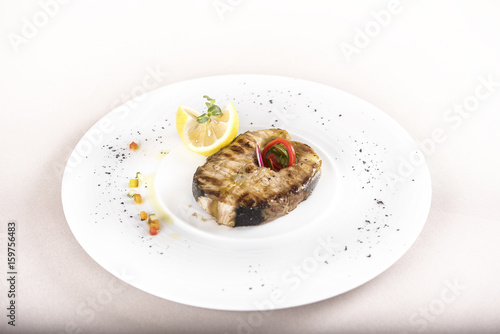 Grilled carp, served with lemon and decorated with radish and fresh leafs, light background, isolated