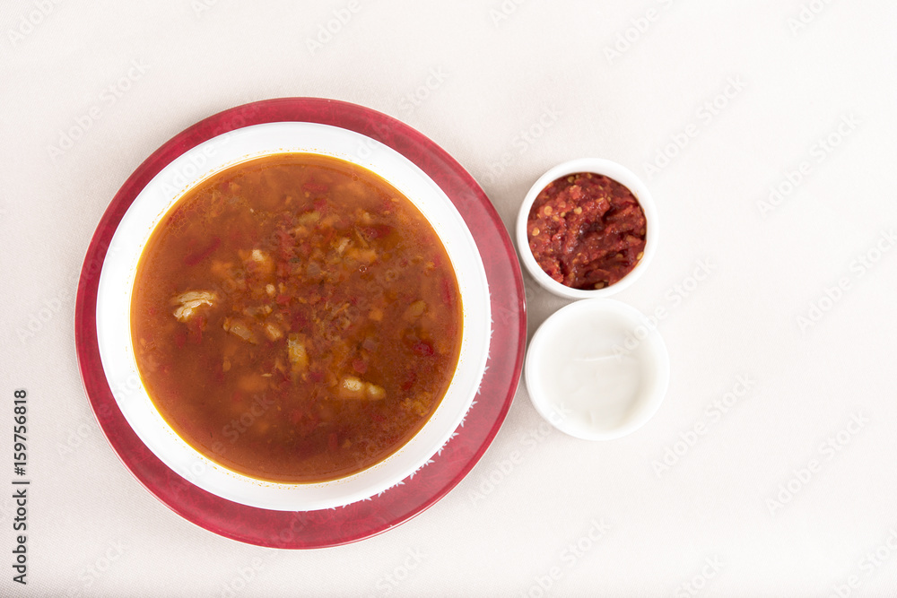 Tomato soup, served with sour cream and extra tomato sauce, white and red plate, light background, isolated Tomato soup, served with sour cream and extra tomato sauce, white and red plate, light background, isolated