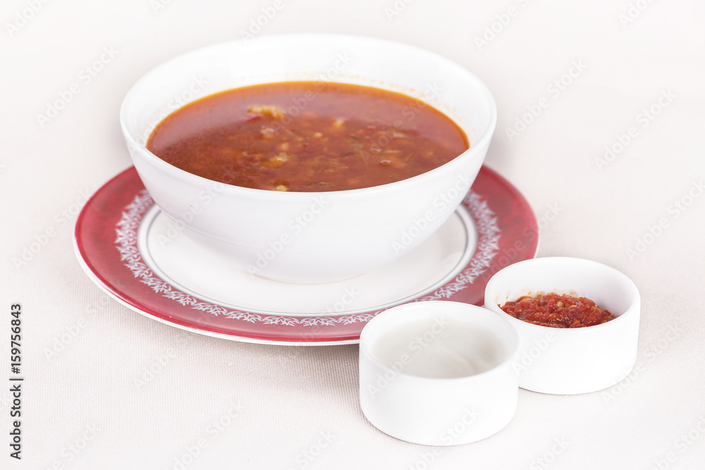 Tomato soup, served with sour cream and extra tomato sauce, white and red plate, light background, isolated Tomato soup, served with sour cream and extra tomato sauce, white and red plate, light background, isolated