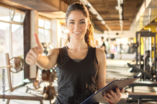 Fotografia Portrait of personal trainer with clipboard showing thumb up at gym