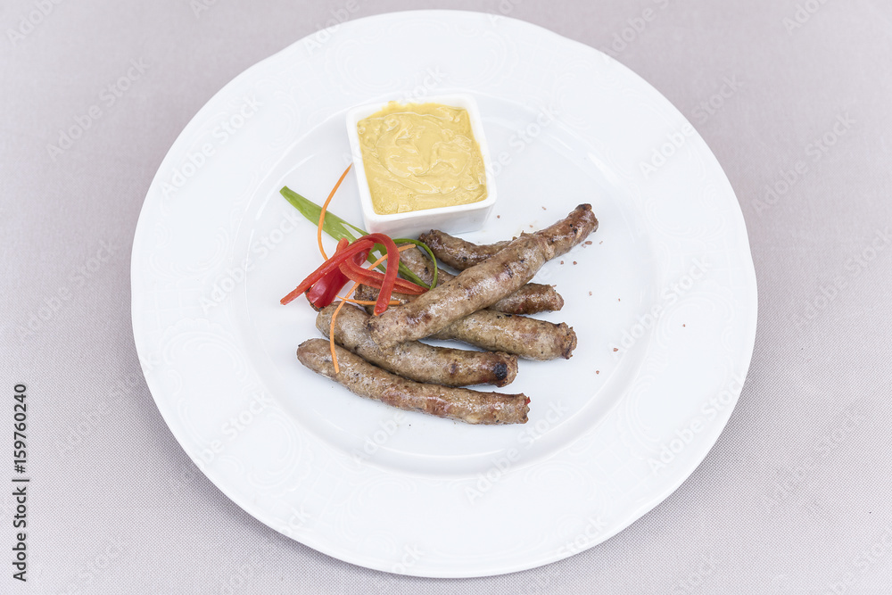 Homemade sausages, served with mustard and decorated with herbs, isolated on light background, white plate
