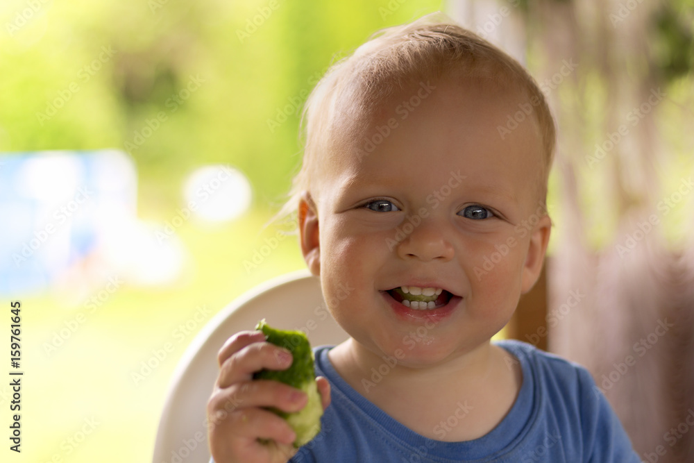 Adorable infant kid with a cucumber in his hand laughing and looking at camera Adorable infant kid with a cucumber in his hand laughing and looking at camera