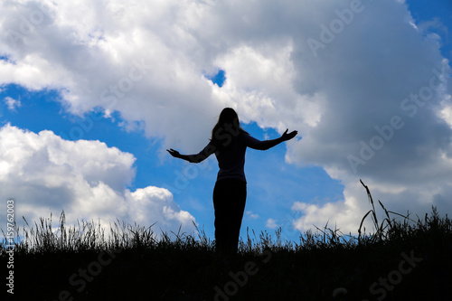 Silhouette young woman open arms on hill