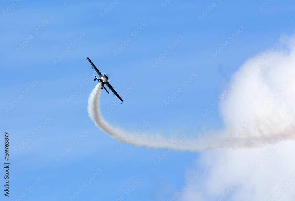 Pilot doing beautiful maneuvers with a propeller plane on a sunny day. White smoke as trail. Blue sky in the background. Pilot doing beautiful maneuvers with a propeller plane on a sunny day. White smoke as trail. Blue sky in the background.