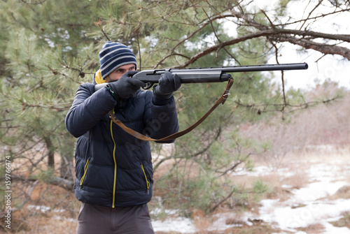 caucasian male in winter forest takes aim. Hunting with a shotgun
