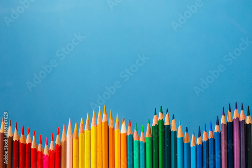 Slika na platnu Colored pencils wave on blue background. Copy space.