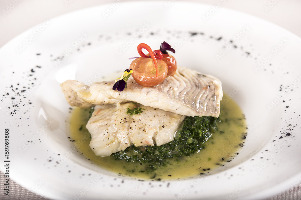 Perch fillet with spinach, sauce and tomato, decorated with eatable flowers and red leafs, placed on white plate, light background, isolated Perch fillet with spinach, sauce and tomato, decorated with eatable flowers and red leafs, placed on white plate, light background, isolated