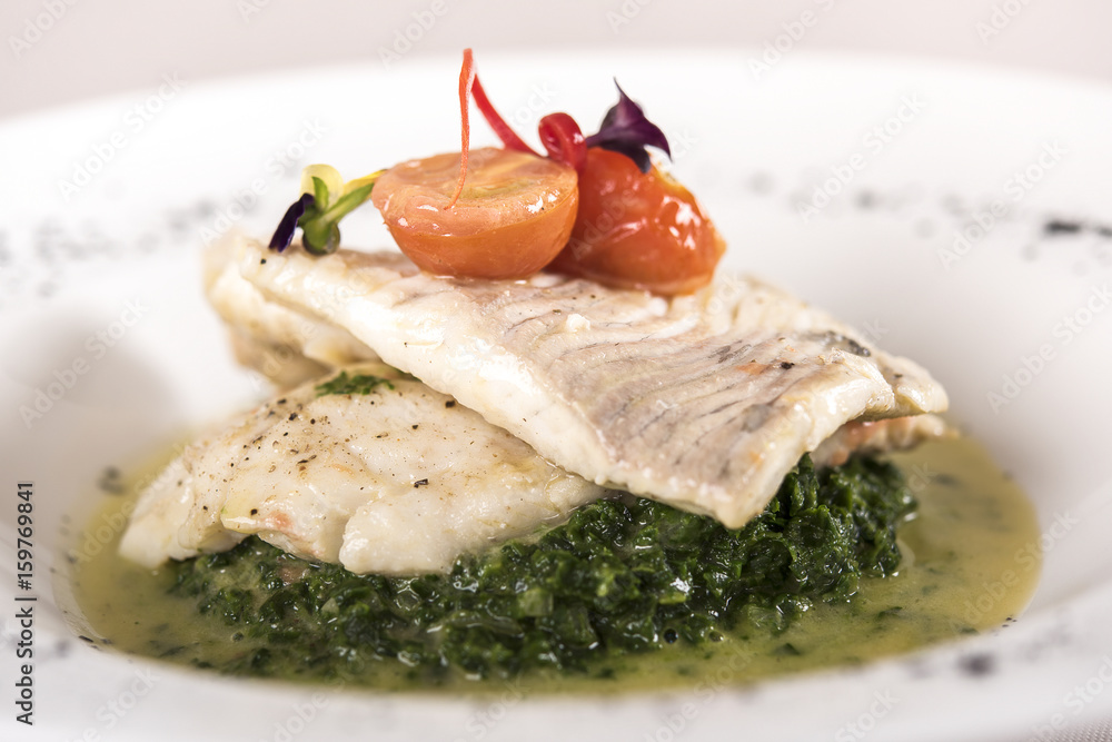 Perch fillet with spinach, sauce and tomato, decorated with eatable flowers and red leafs, placed on white plate, light background, isolated Perch fillet with spinach, sauce and tomato, decorated with eatable flowers and red leafs, placed on white plate, light background, isolated
