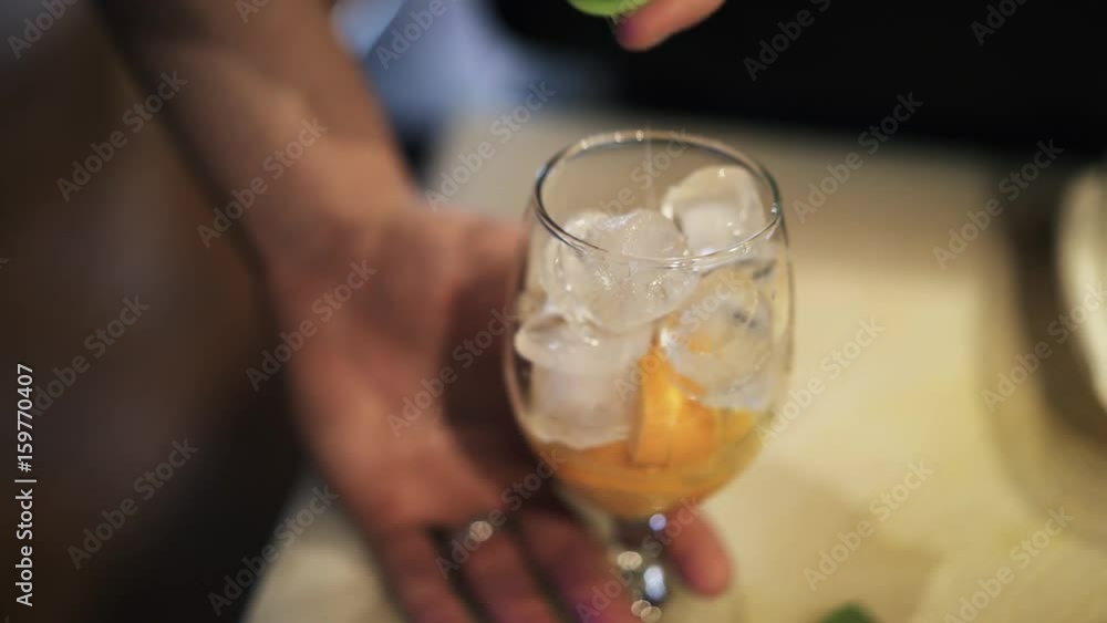 Close up of a hand of an unrecognizable bartender s hands adding alcohol into a glass with a slice of lemon and ice cubes. Handheld real time close up shot Close up of a hand of an unrecognizable bartender s hands adding alcohol into a glass with a slice of lemon and ice cubes. Handheld real time close up shot