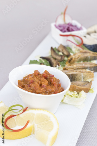 Plate with various types of fish, smoked and marinated, served with fresh salad, vegetable salad, onion salad, decorated with herbs, isolated on light background, white plate