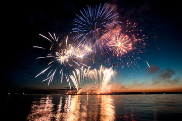 Holiday fireworks above water with reflection on the black sky background