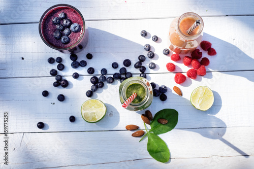  Blueberry, spinachy and orange smoothie on a wooden white background in nature. Glasses of smoothie with berry and mint. Berry, leaf and lime, raspberries on a table. Fruit Healthy food. 