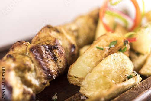 Pork skewers served with baked potatoes, Coleslaw salad and barbecue sauce, decorated with radish, red and green herbs, placed on a wooden plate, light background, isolated photo