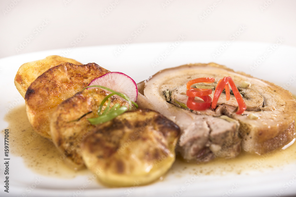 Slice roasted pork, served with potatoes and decorated with herbs, placed on white plate, light background, isolated