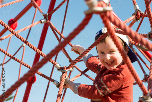 Young boy child playing at outdoor playground climbing net