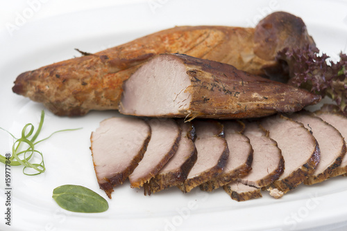 Pork tenderloin, decorated with green and red leafs, placed on a white and red plate, light background