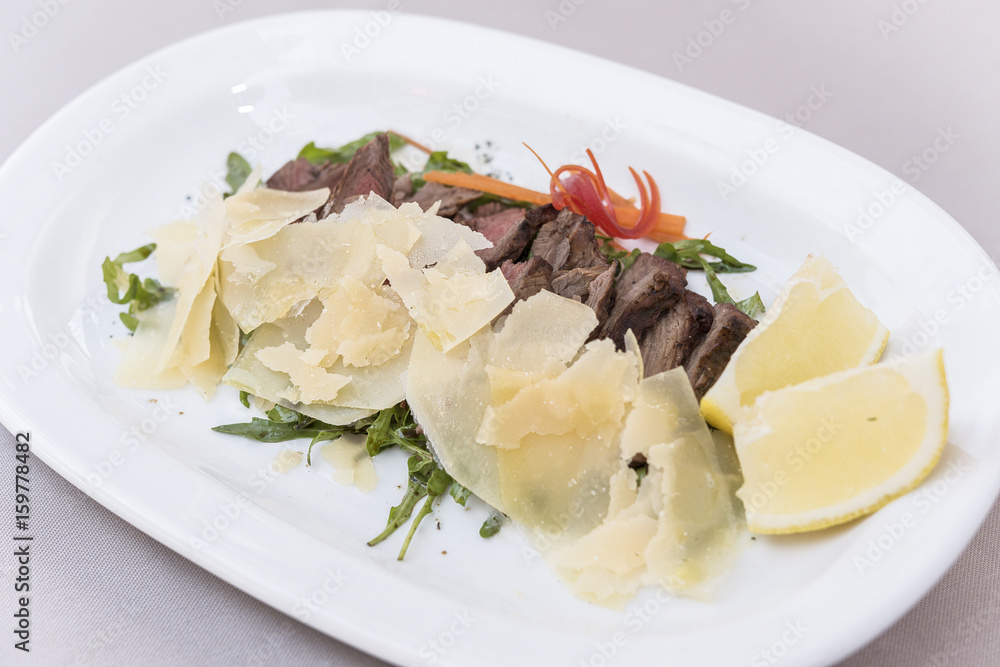 Fresh appetizer with prosciutto ham and slices of parmesan, decorated with green leaf, placed on white plate, light background, isolated Fresh appetizer with prosciutto ham and slices of parmesan, decorated with green leaf, placed on white plate, light background, isolated