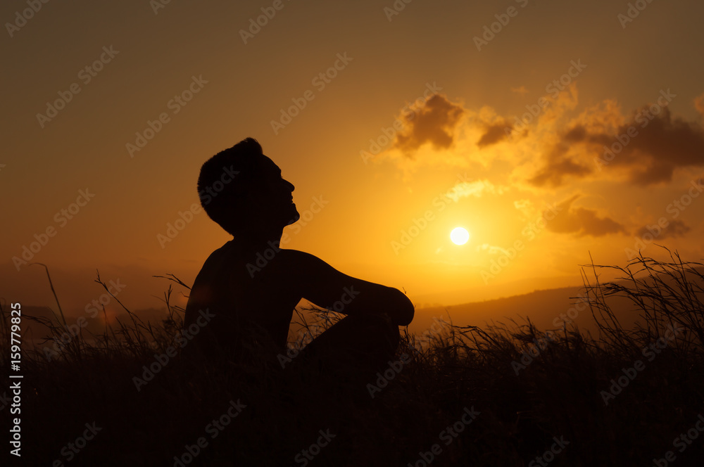 Young man sitting in nature looking up into the sky enjoying the beautiful sunset. 