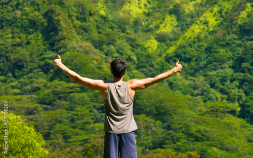 Young man standing on a mountain with thumbs up in the air. Healthy active lifestyle and fitness concept. 