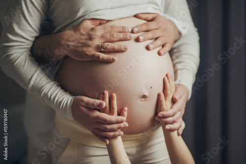 Руки ребенка и родителей держат живот беременной женщины photo