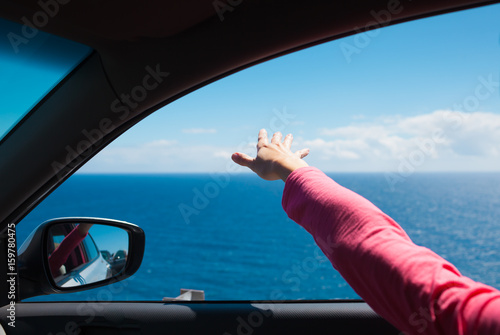 Road trip. Woman in her car enjoying the ocean breeze trough her finger tips