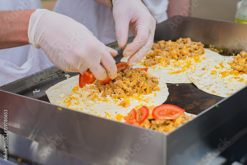 Close-up of hands of cook in gloves preparing fresh fajita. Healthy fresh tortillas with grilled chicken fillet, cheese. Concept of national food, healthy fast food photo