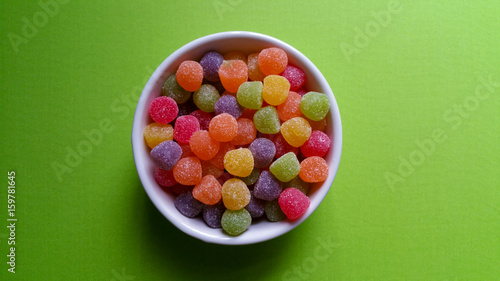 Sweet jujubes in white pot over green background top view