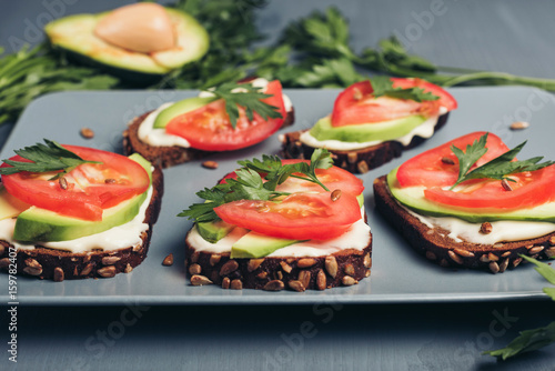 Healthy green veggie food concept. Yammy toast with cream cheese, avocado and juicy red tomato on grey table.