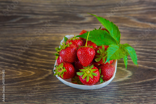 A small white porcelain bowl filled with juicy fresh ripe red strawberries. Textured table top. Fresh strawberries. Strawberries in a Bowl