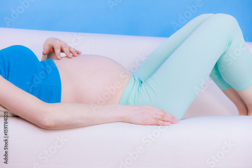 Pregnant woman lying on couch touching her belly © Voyagerix